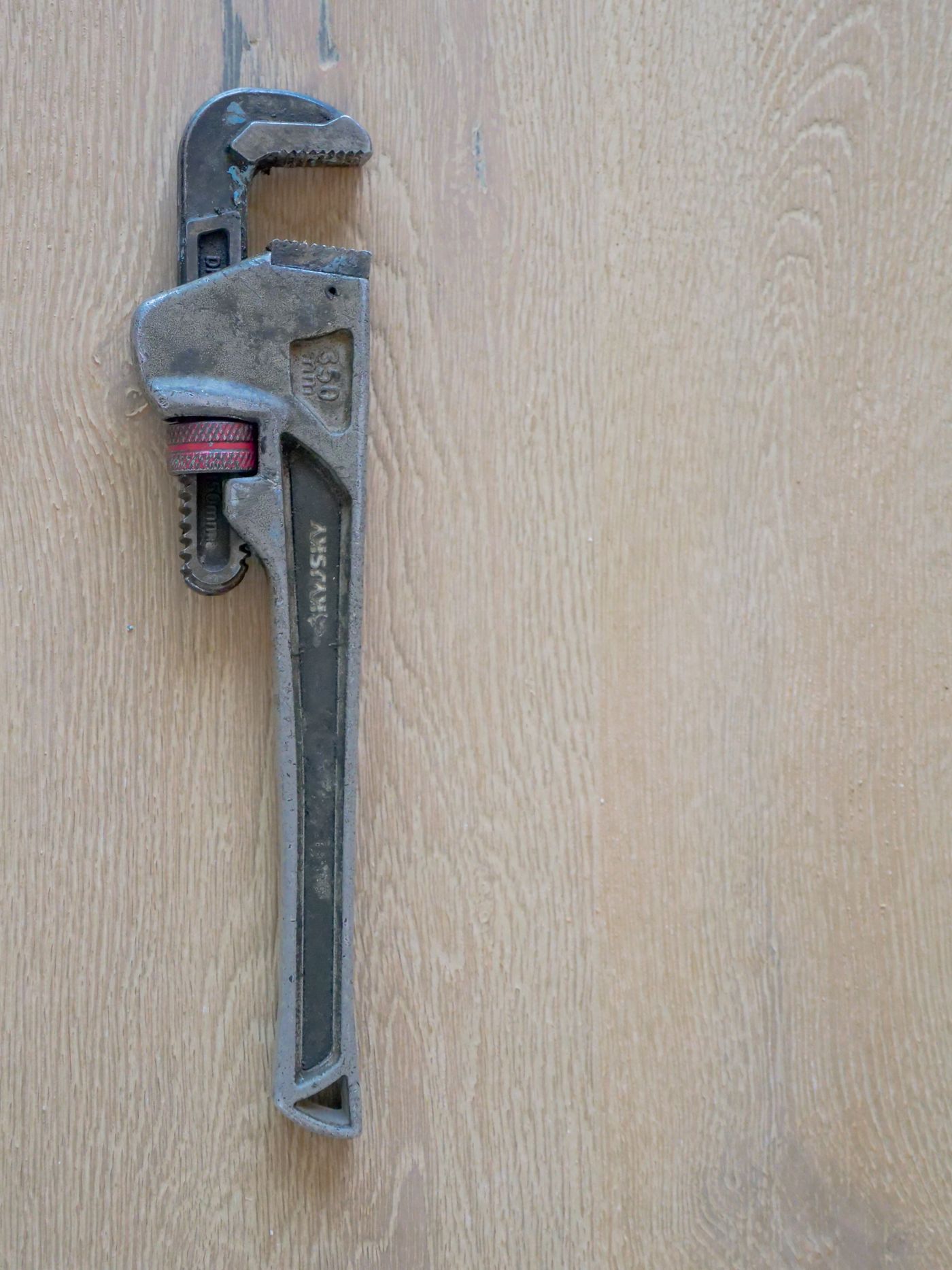 A steel pipe wrench lying on a wooden surface